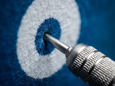 Metal dart tip landing in the bullseye of a blue and white fabric target